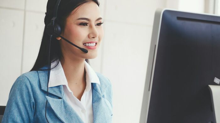 A smiling woman wearing a headset and looking at a computer, showcasing a positive attitude for amazing comebacks.
