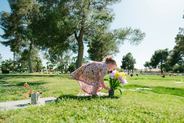 A child in a floral dress places flowers on a grave, a poignant image of unsettling childhood memories.