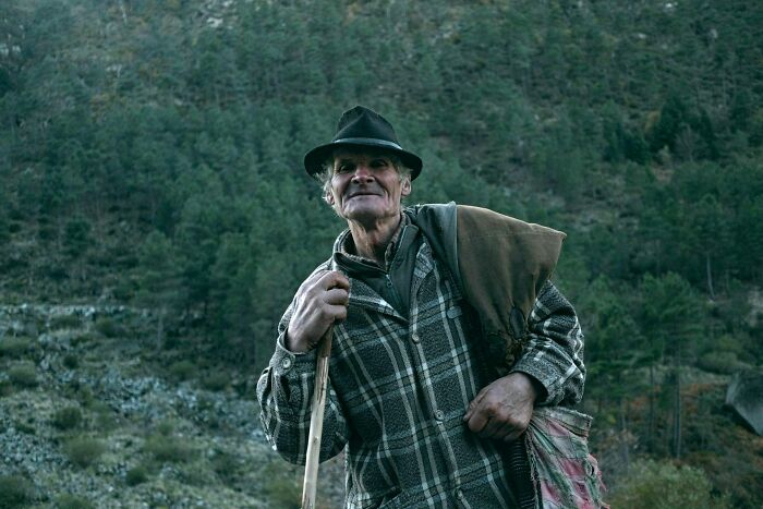 An elderly man in a hat and plaid coat with a stick, representing unsettling childhood memories.