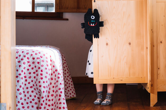 A child's legs and a black monster puppet peek from behind a wooden partition, an image that can stir unsettling childhood memories.