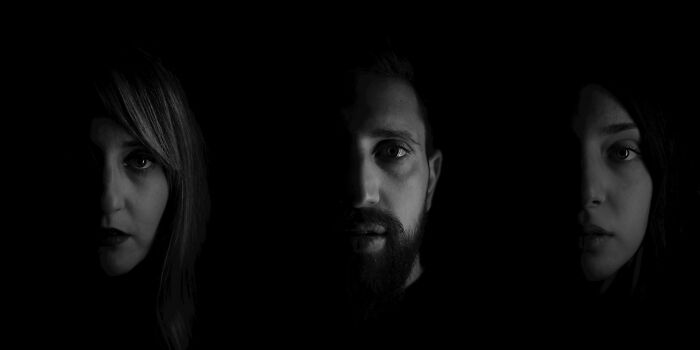 Three faces partially emerge from complete darkness, representing unsettling childhood memories.