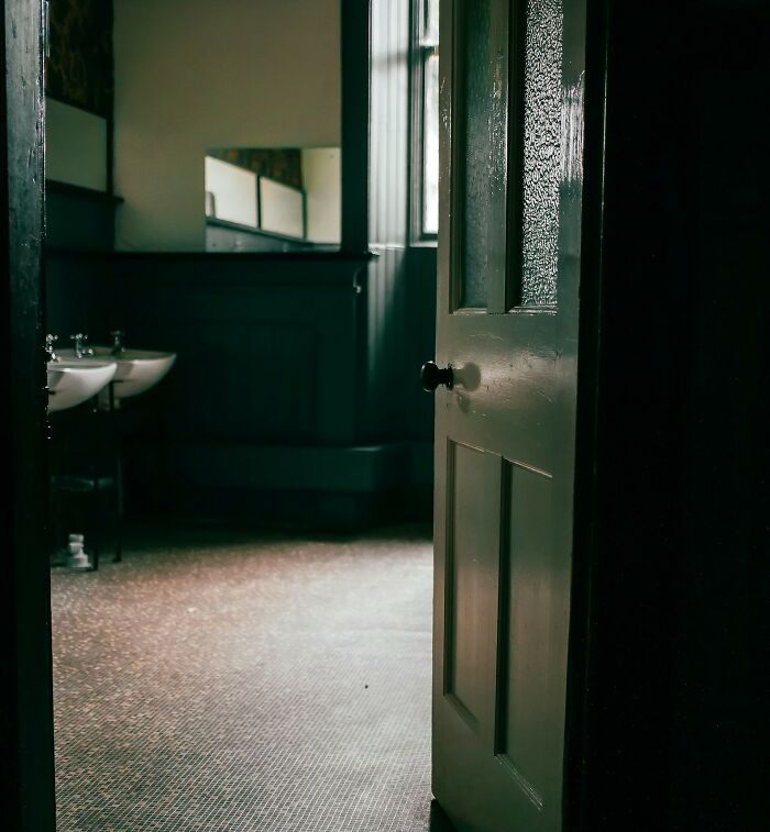 A slightly ajar door opens to a dark bathroom, evoking unsettling childhood memories.
