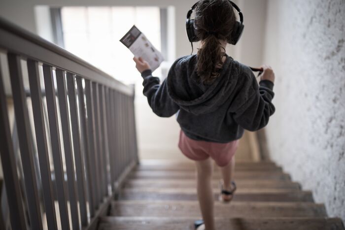 A young girl with headphones walks down wooden stairs, perhaps experiencing unsettling childhood memories.