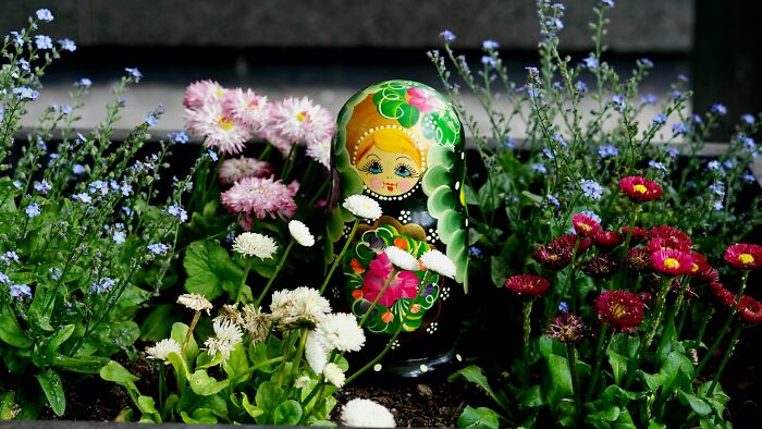 A colorful nesting doll surrounded by flowers, evoking unsettling childhood memories.