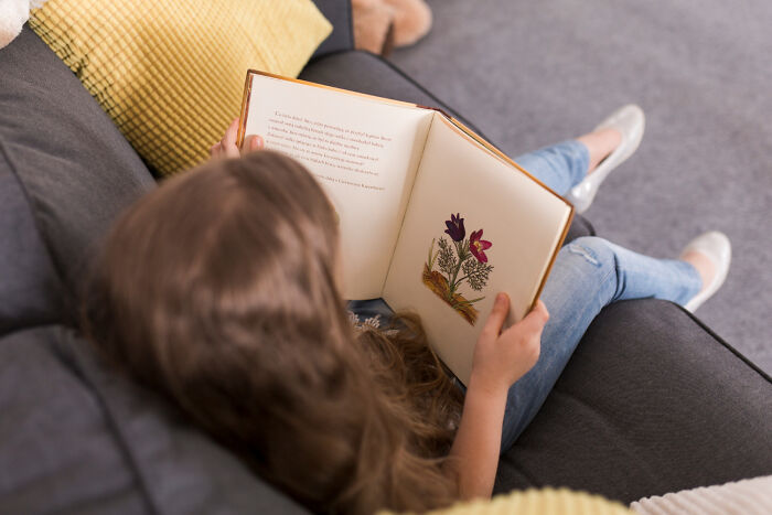 A young girl reading a book on a couch, illustrating unsettling childhood memories that still give people chills.