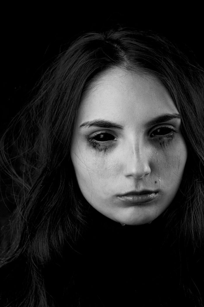 A black and white close-up of a person with dark eyes and tear streaks, conveying unsettling childhood memories.