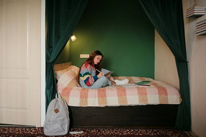 A person sitting on a bed writing, surrounded by dark curtains, suggesting unsettling childhood memories.