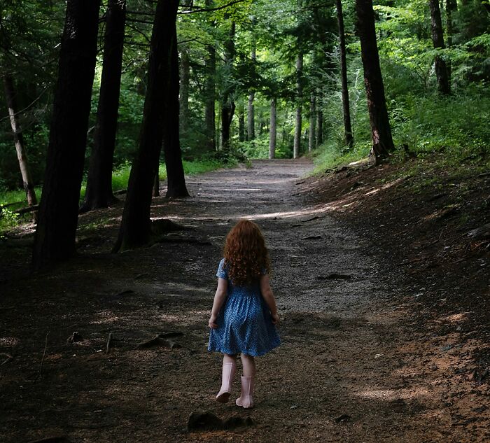 A young girl with red hair walking on a forest path, evoking unsettling childhood memories and chills.