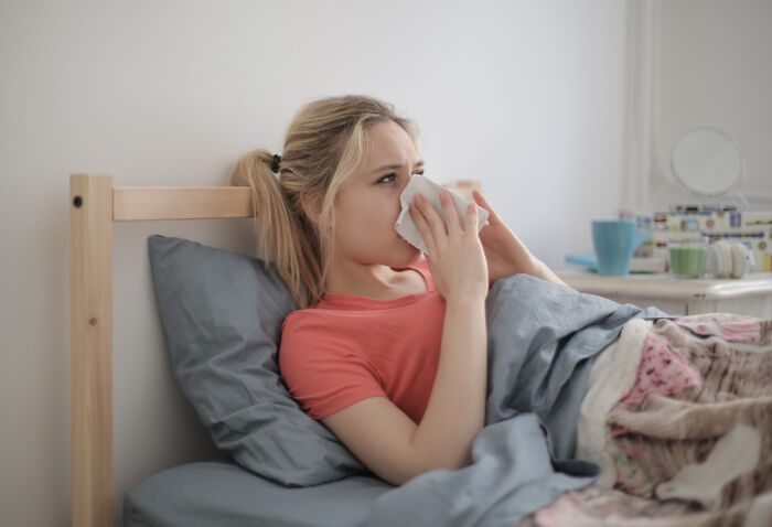 A woman lies in bed, blowing her nose, possibly due to unsettling childhood memories keeping her awake.