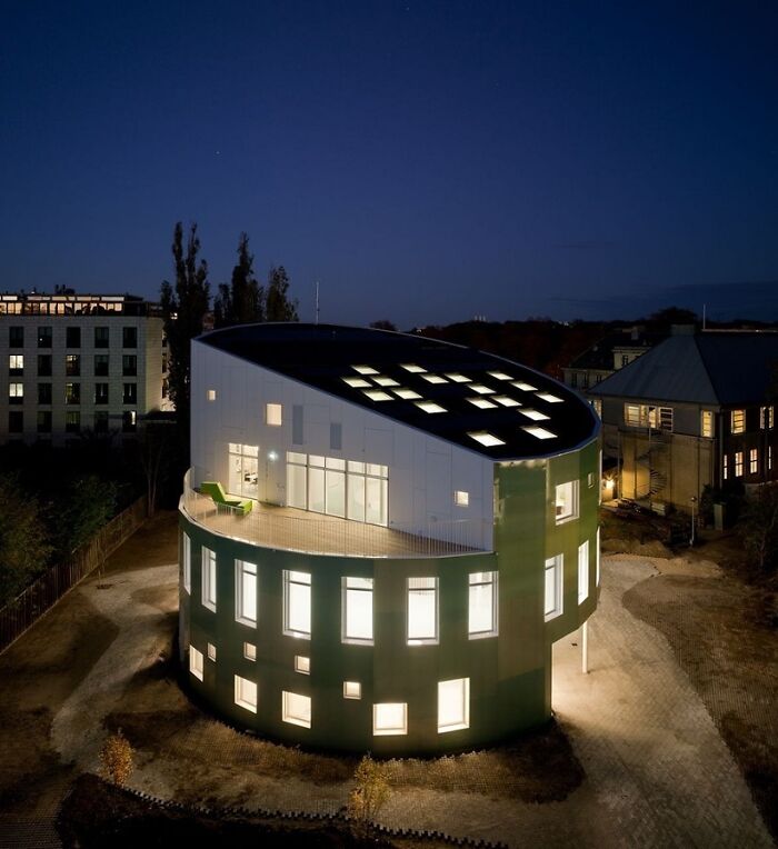 An evening view of a circular building with a green base and light-filled windows, a brilliant design choice surprising people.