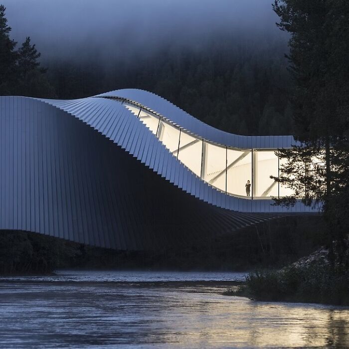 A modern, wavy brilliant design building with illuminated windows spanning a dark river.