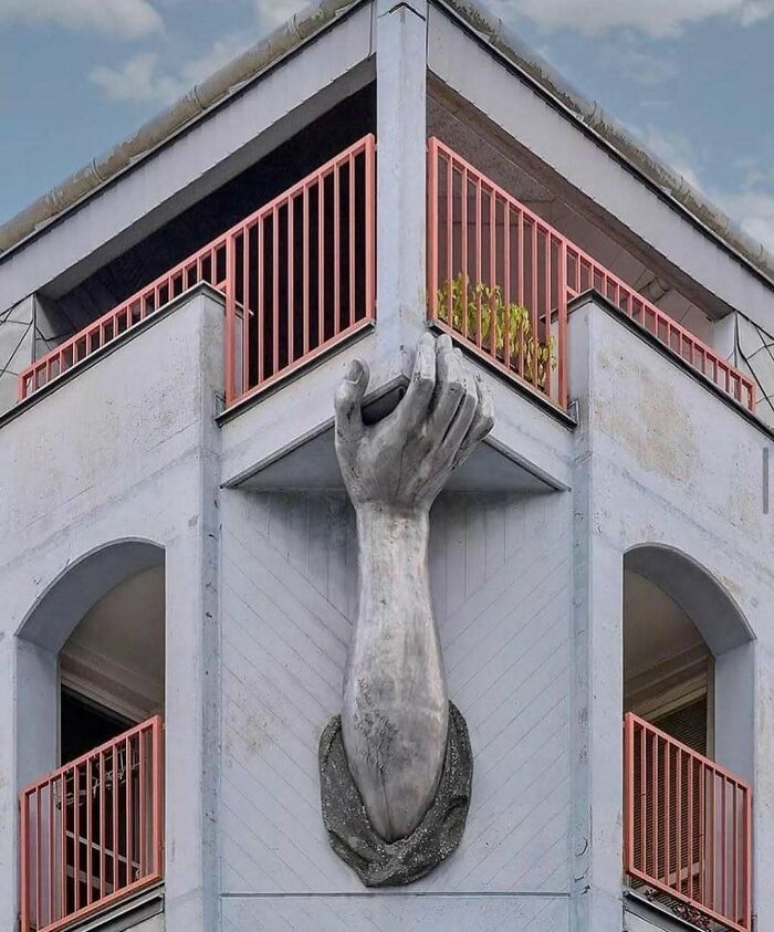A building corner with a large sculpted hand holding the edge, demonstrating brilliant design choices.