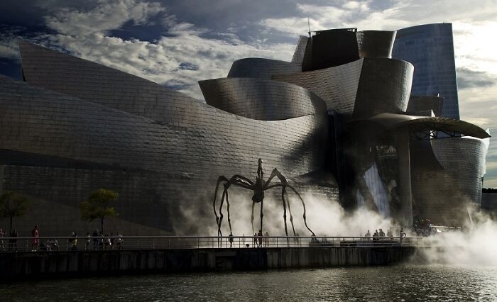 An architectural masterpiece with brilliant design choices, a large modern building and a giant spider sculpture with fog.
