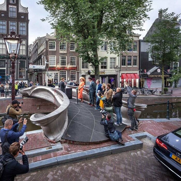 People gathering around a futuristic-looking metal bridge in a city, highlighting brilliant design choices.