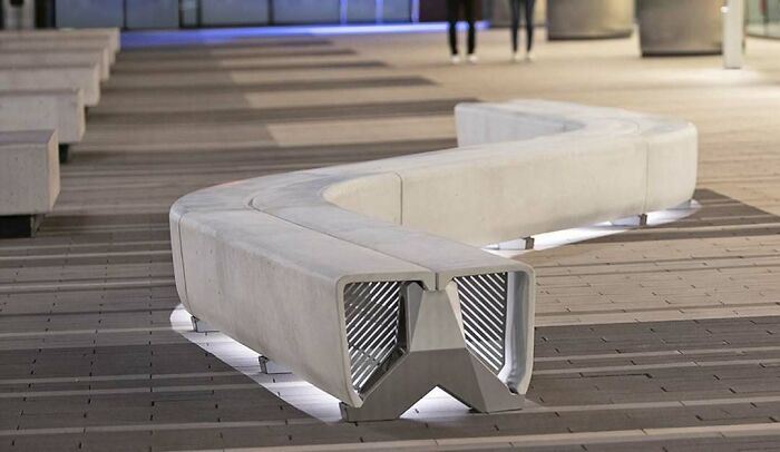 A brilliant design choice for a modern S-shaped concrete bench with subtle lighting on a paved walkway.