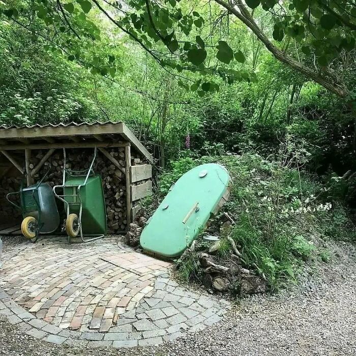 A green boat repurposed as a garden bed next to a woodpile, illustrating brilliant design choices in landscaping.