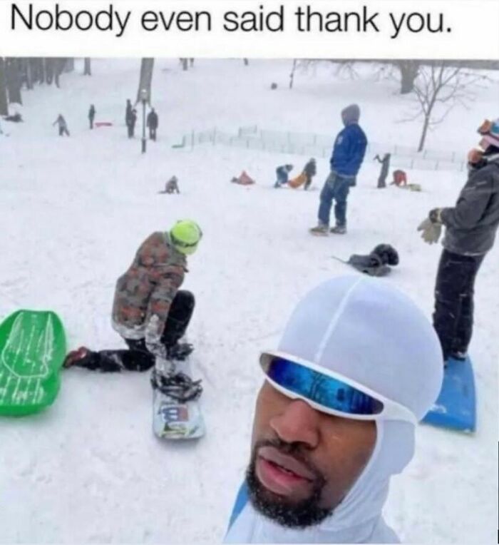 A man in white goggles taking a selfie with people sledding and snowboarding in the background, a funny pop culture post.