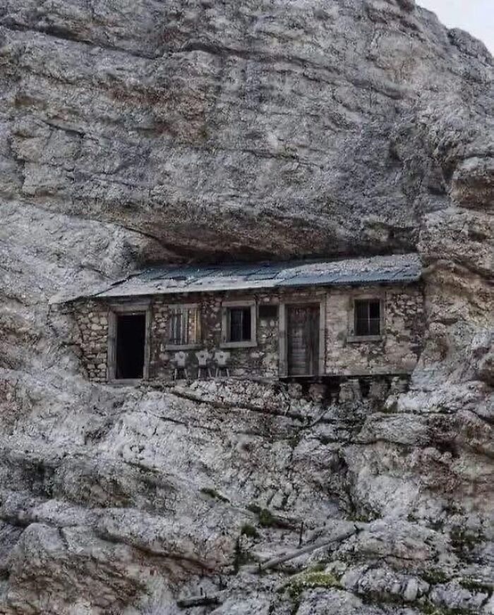 A small, rustic house built into a sheer rock face, presenting a fascinating fact about unique architecture.