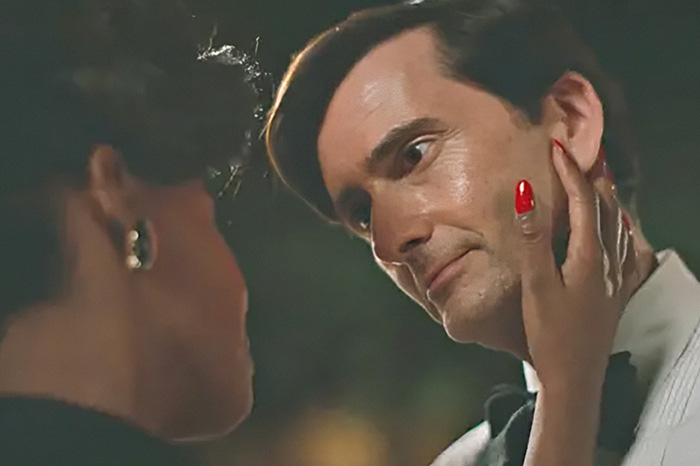 A behind-the-scenes look at an intimate scene showing a woman caressing a man's face.