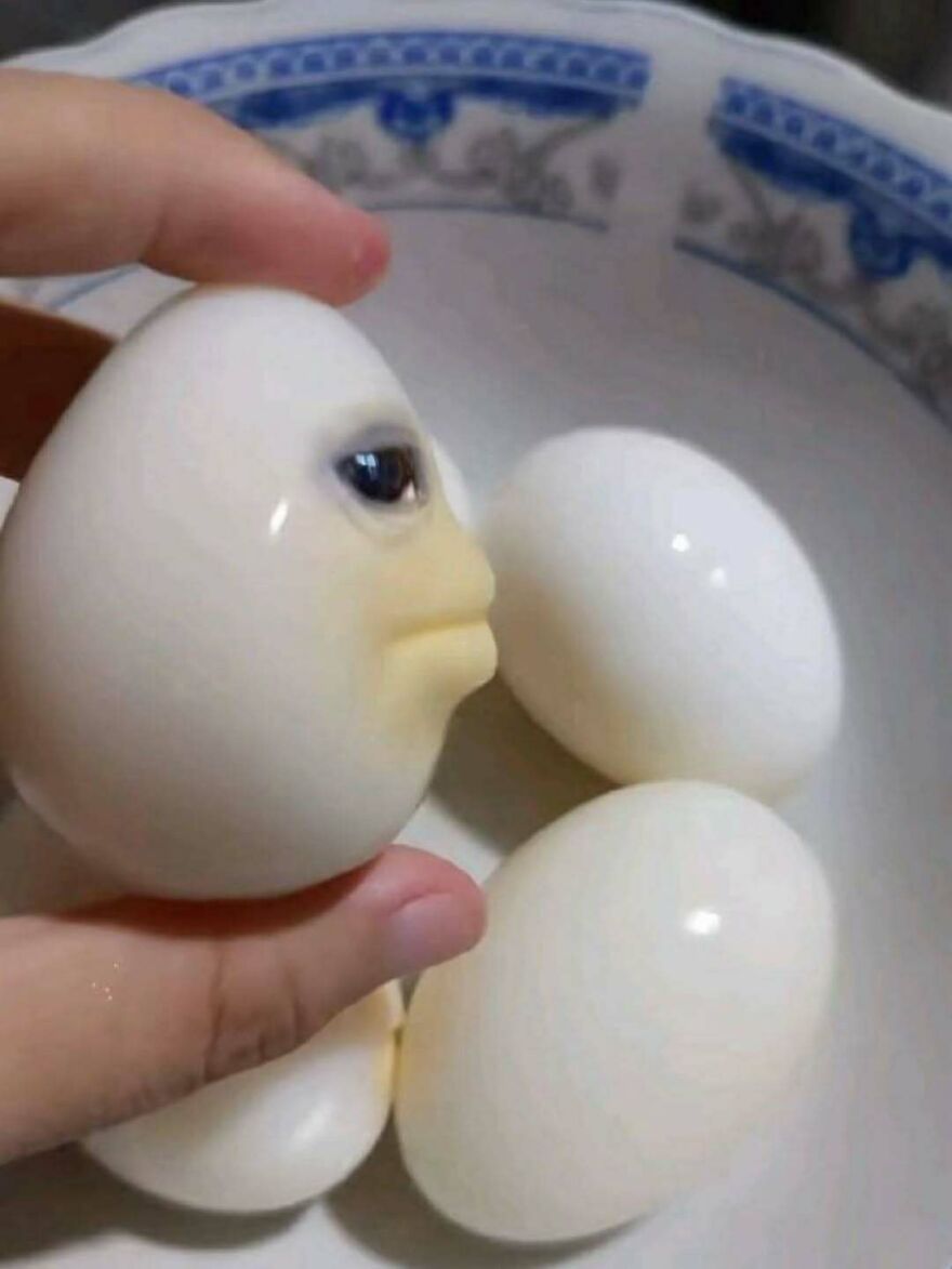 A weird person made a hard-boiled egg with a face sculpted into it among other plain eggs.