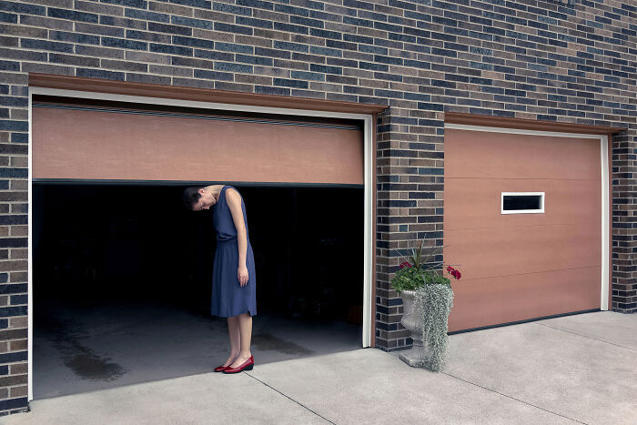 A photographer creates surreal images of a woman bending beneath a garage door, making the scene uncanny. Everyday places.