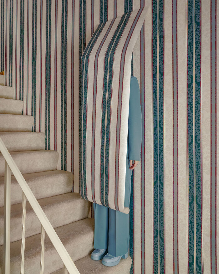 A photographer creates surreal images; a person in blue stands concealed by a roll of wallpaper in an uncanny hallway.