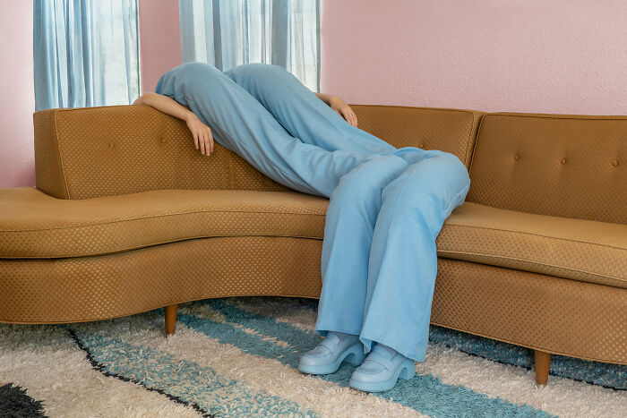 A person in light blue pants appears to be melted over a brown couch, creating a surreal and uncanny image.