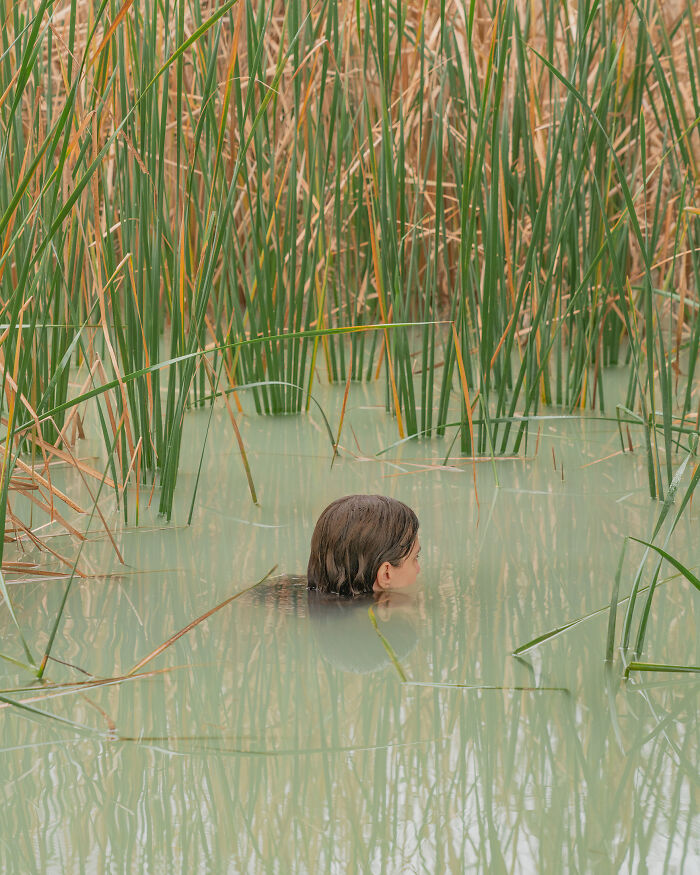 A photographer creates surreal images; a person's head emerges from murky water among tall, green reeds, feeling uncanny.