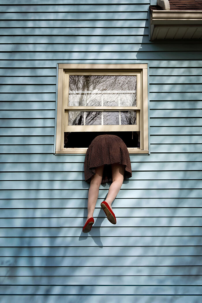 A photographer creates surreal images; a person's legs are seen hanging out of a window on a blue house.