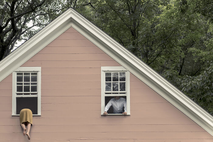 A photographer creates surreal images; a person peeks out of a window while another hangs out of an adjacent window.
