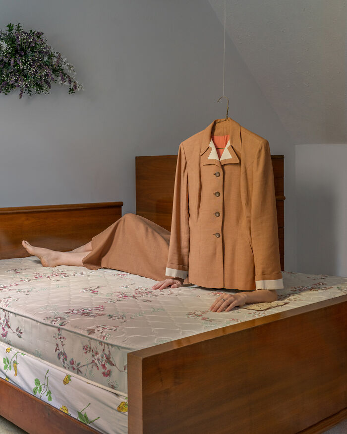 A jacket on a hanger seemingly standing on a mattress with a person's legs and hands visible, a surreal image.