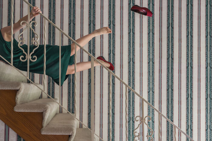 A woman in a green dress and red shoes appears to fall backward up a staircase in this surreal image.