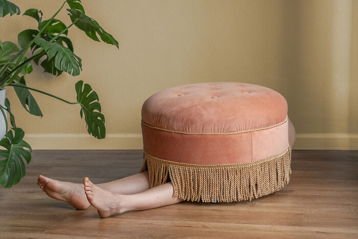 A person with legs sticking out from under a pink ottoman, creating a surreal image in an everyday place.