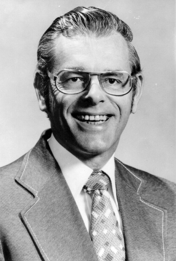 A black and white photo of a smiling man in glasses, one of the mysteries where people know who is to blame.