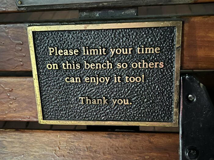 A sign on a wooden bench asks users to limit their time, a design choice showing urban designers forgot comfort.