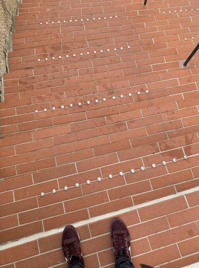A pair of feet stand at the bottom of a brick staircase with studded discomfort, showing urban designers forgot comfort.