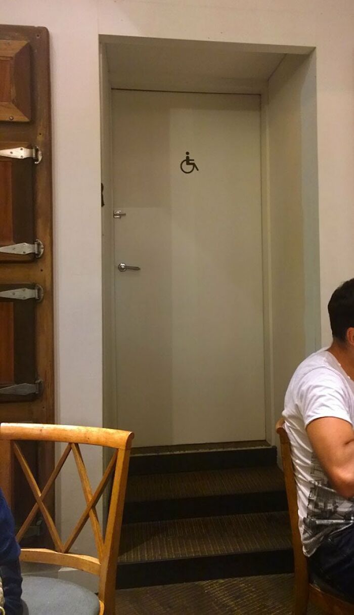 A white door with a wheelchair symbol is placed at the top of a short staircase, highlighting poor urban design.