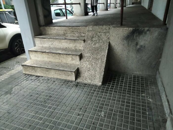 A short, steep, broken concrete ramp next to stairs, highlighting the neglect of accessibility by urban designers.