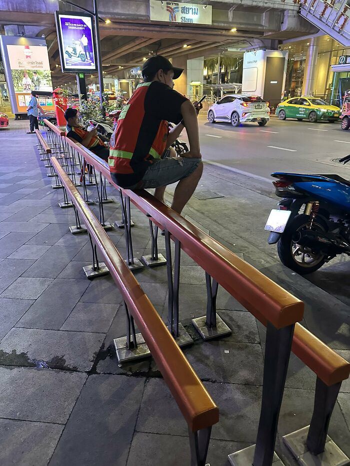Urban designers forgot about people's comfort; a man sitting on a narrow, uncomfortable railing next to a street.
