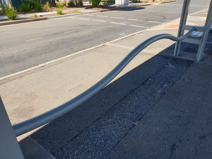 Urban designers forgot about people's comfort; a bent, unsupportive metal bar intended for seating at a bus stop.