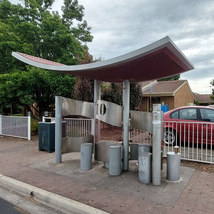A modern, uninviting bus stop with metal pillars and a curved roof, reflecting poor urban design for people's comfort.