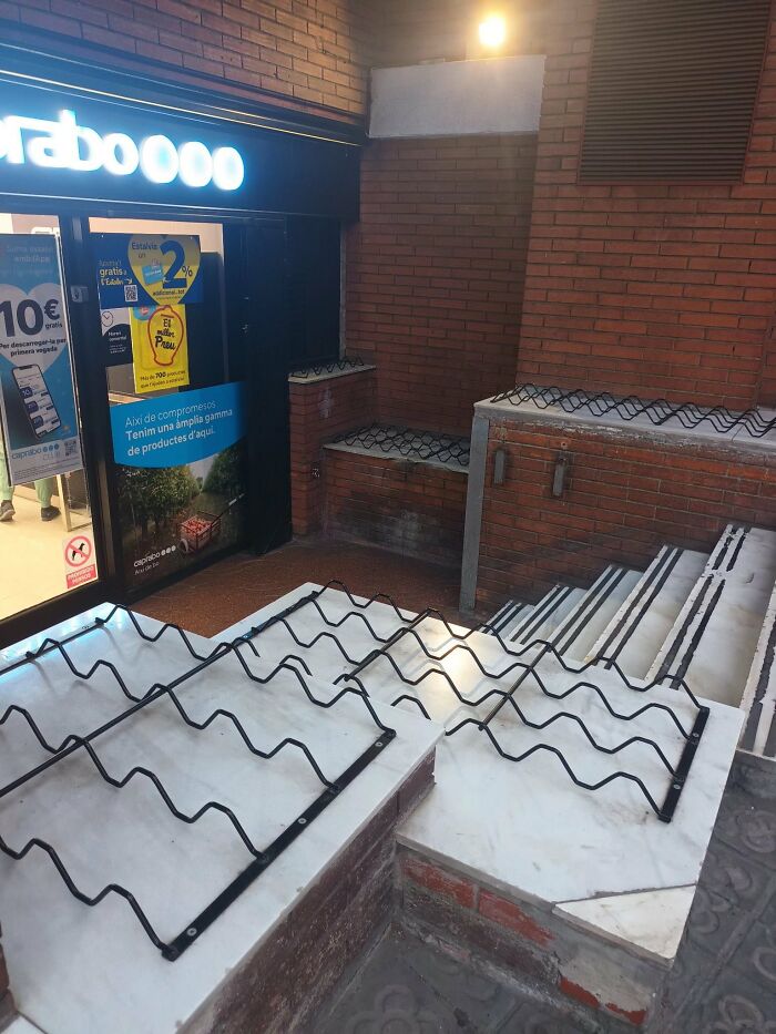 A building entrance with jagged metal structures on ledges and stairs, a poor urban design choice impacting comfort.