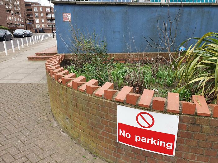 A low brick wall with a No Parking sign, demonstrating urban design forgetting people's happiness.