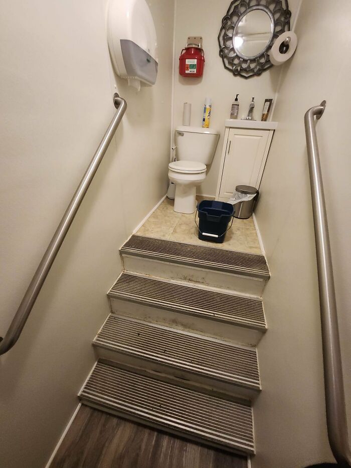 A toilet at the top of a short, narrow staircase, with handrails, reflecting urban designers' oversight in people's comfort.