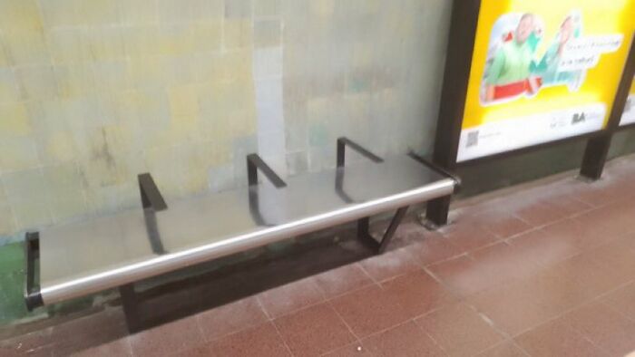 A narrow metal bench with two dividers designed by urban designers, making it uncomfortable for people to lie down.