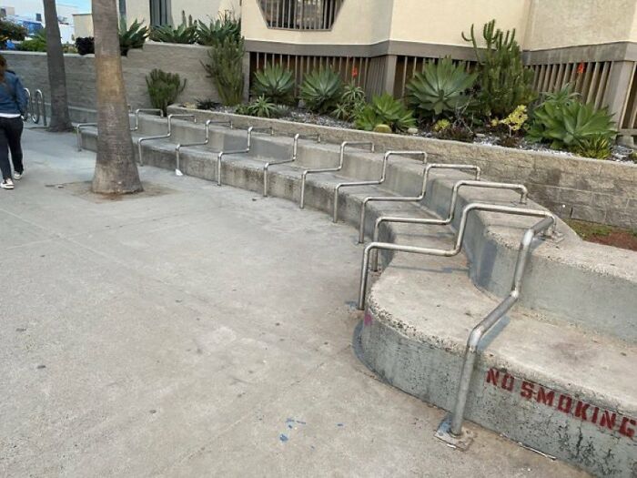 Concrete steps with multiple metal handrails installed by urban designers, obstructing people's comfortable use of the space.
