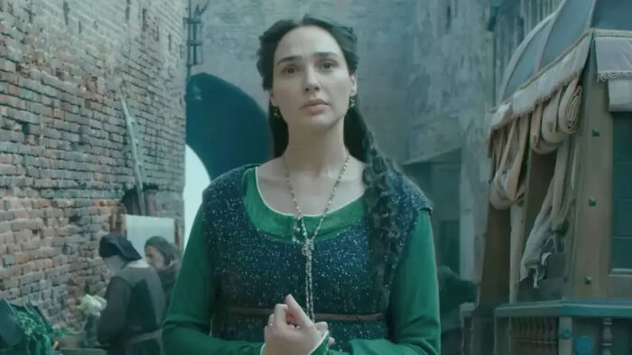 Gal Gadot in historical attire, looking serious in an old European street setting, from her new Netflix film.