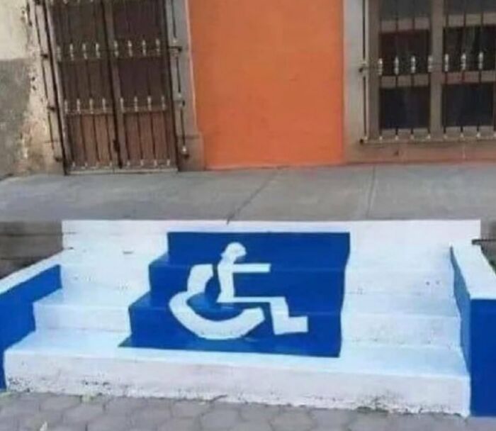 A blue and white ramp with a disability symbol, but made of stairs, an example of urban designers forgetting comfort.