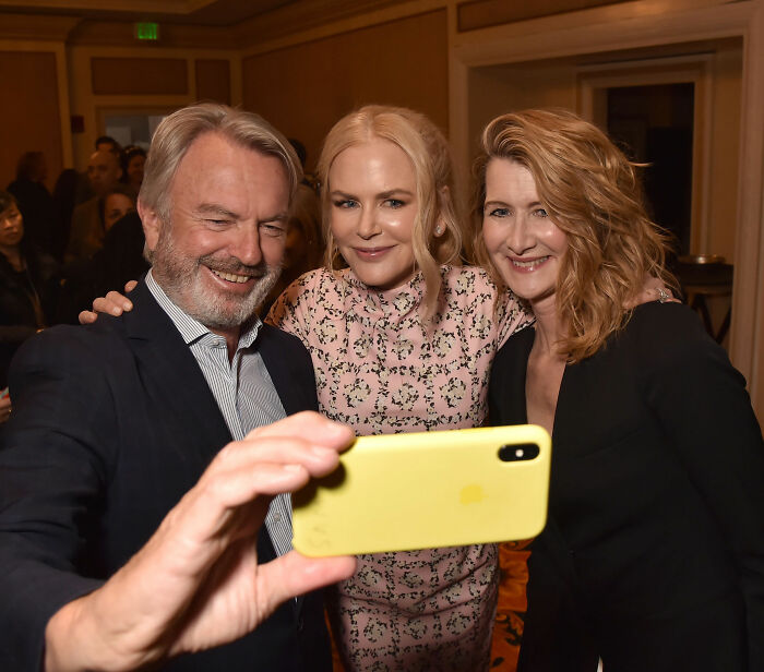 Sam Neill takes a selfie with Nicole Kidman and Laura Dern at an event, smiling broadly. Sam Neill takes a selfie with Nicole Kidman and Laura Dern at an event, smiling broadly.