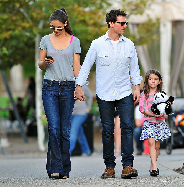 Katie Holmes, Tom Cruise, and Suri Cruise walking outdoors, emphasizing Suri's legal action against her father.